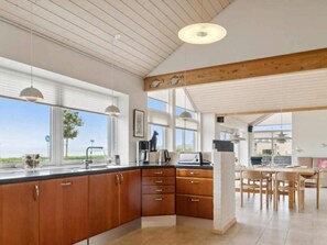 Una cocina moderna con armarios de madera, un comedor con mesa y sillas, y ventanas amplias que ofrecen vistas.