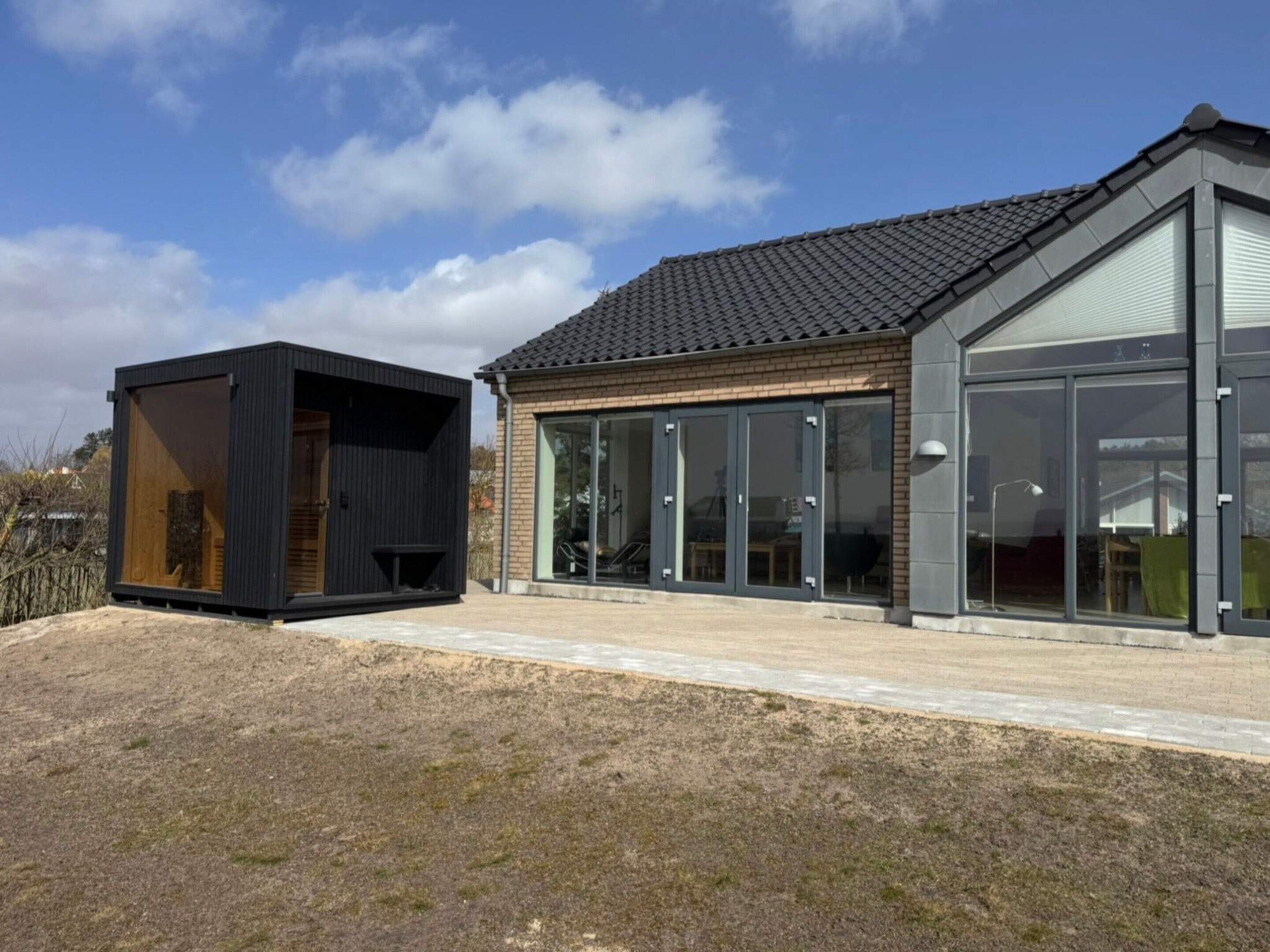 A modern house with a large glass door, a small wooden structure, and a tiled roof.