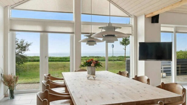 A spacious dining area with a large table, chairs, a hanging light fixture, and a TV mounted on the wall. - 4 Star Holiday Home in Ebeltoft (Ebeltoft)