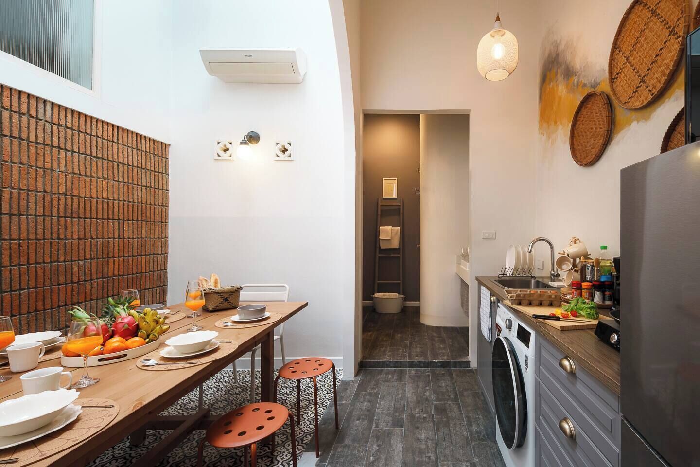 A compact kitchen with a washing machine, a dining area with a table set for two, and a small bathroom visible in the background.