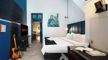 A modern hotel room with a bed, a desk, a guitar, a TV, and a painting on the wall.