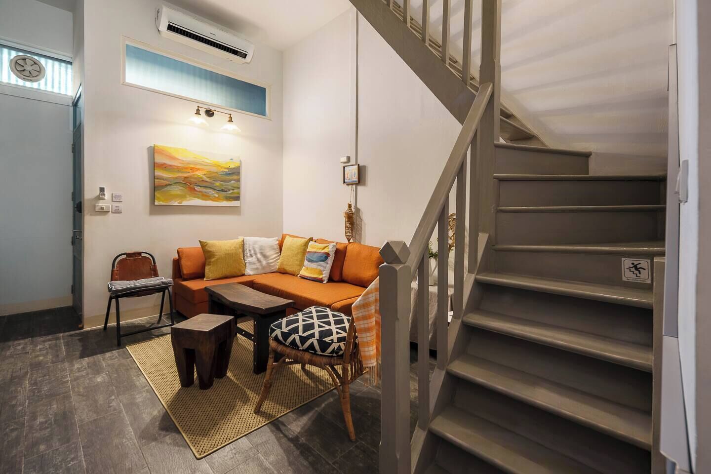 A living room with a sofa, chairs, a coffee table, a staircase, and a painting on the wall.