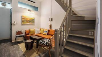 A living room with a sofa, chairs, a coffee table, a staircase, and a painting on the wall.