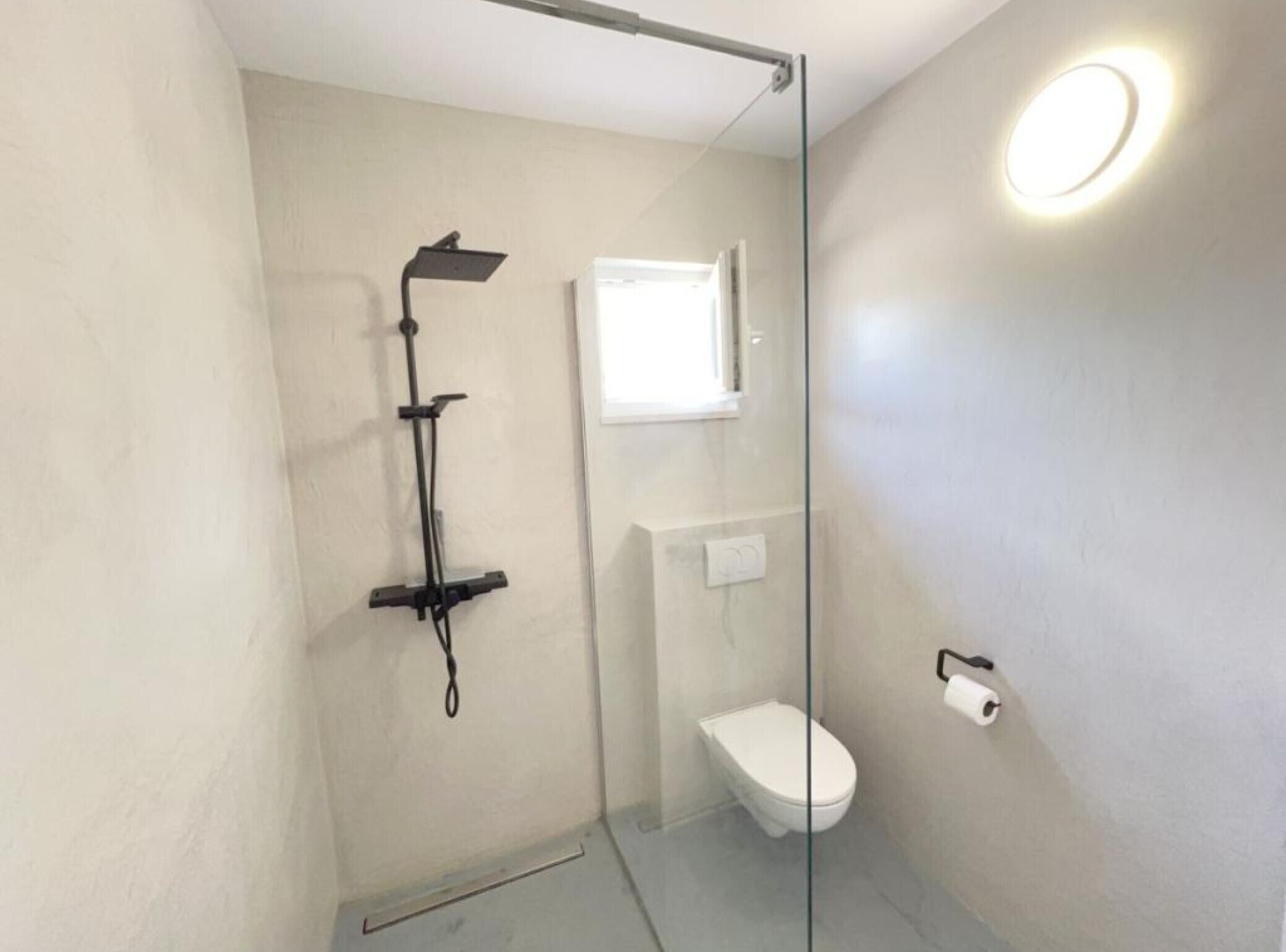 Ein kleines, modernes Badezimmer mit Duschkabine aus Glas, Toilette und wandmontiertem Waschbecken.