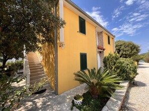 A yellow building with a staircase, green shutters, and a stone wall. - One bedroom apartment with sea view (1) (Loviste)