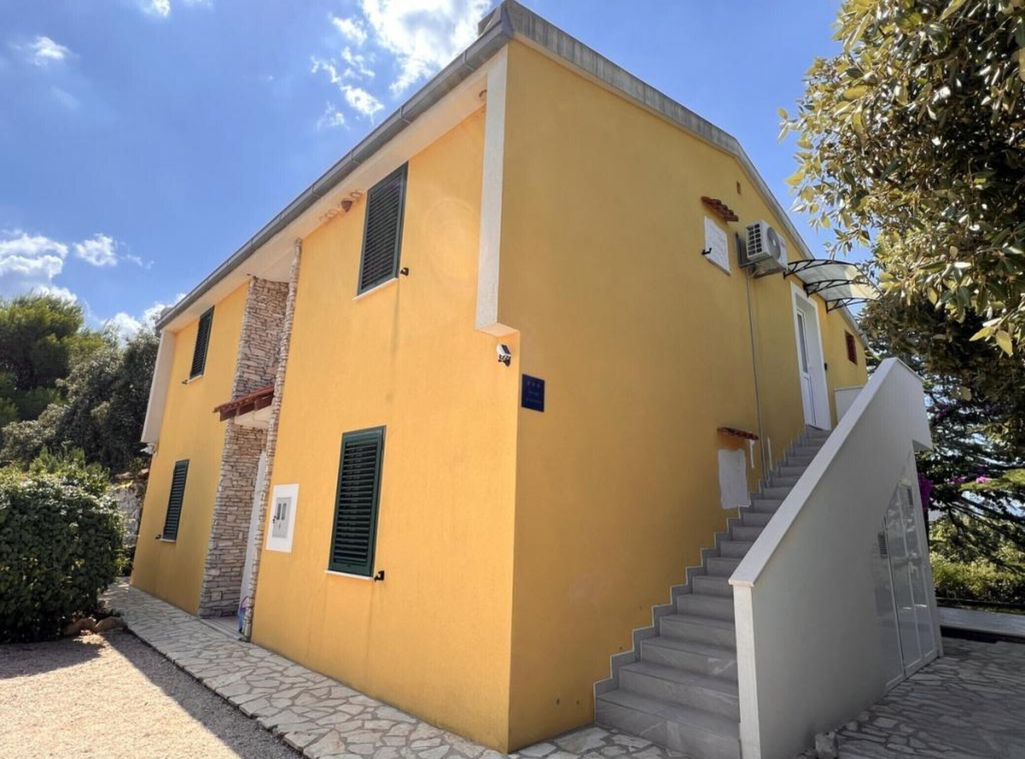 Un bâtiment jaune avec une façade en pierre, un escalier et une petite porte.