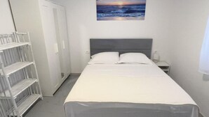 Una camera da letto con un letto, un comodino, un armadio e un quadro raffigurante un tramonto sul mare.