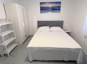 Ein Schlafzimmer mit einem Bett, einem Nachttisch, einem Kleiderschrank und einem Gemälde, das einen Sonnenuntergang über dem Meer zeigt.
