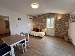 Ein Zimmer mit Stewand, einem Bett, einem Tisch mit Stühlen und einer Klimaanlage.