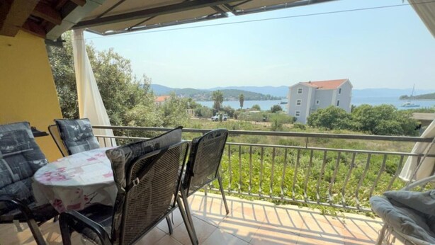 Un balcon avec une table et des chaises, offrant une vue panoramique sur un lac et des bâtiments.