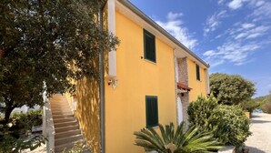 Un bâtiment jaune avec un escalier, des volets verts et un mur en pierre.