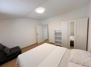 A bedroom with a bed, a wardrobe, a shelf unit, and a door leading to another room. - One bedroom apartment with sea view (4) (Loviste)