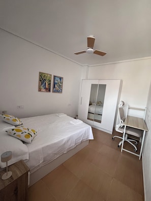 A bedroom with a bed, a desk, a chair, a wardrobe, and a ceiling fan.
