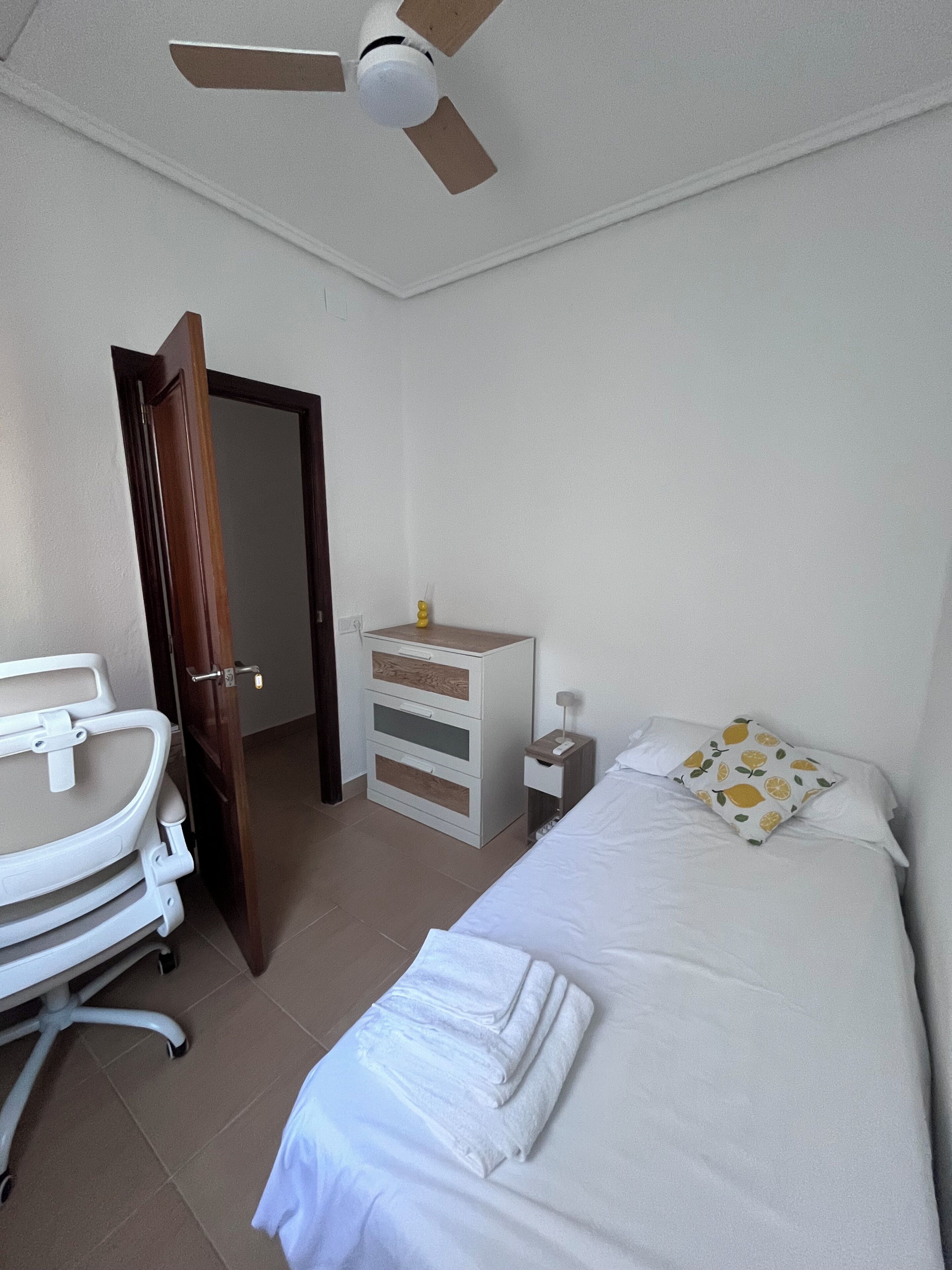 Ein Hotelzimmer mit Bett, Nachttisch, Schreibtisch und Stuhl sowie einem Deckenventilator.
