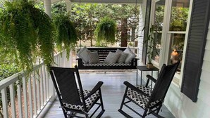 Eine Veranda mit zwei Schaukelstühlen, einem kleinen Tisch und einer hängenden Pflanze.