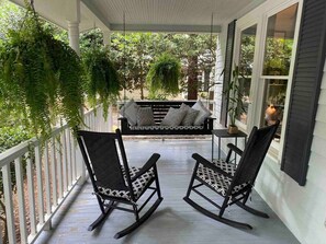 Eine Veranda mit zwei Schaukelstühlen, einem kleinen Tisch und einer hängenden Pflanze.