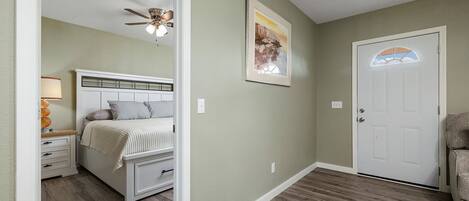 Un dormitorio con cama, mesita de noche, lámpara, ventilador de techo y una puerta.