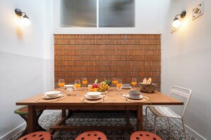 A dining table set with plates, glasses, and a fruit bowl, against a brick wall with a window above. - The Post and Jewelry · Two Best Sellers, One Booking (Bang Rak)
