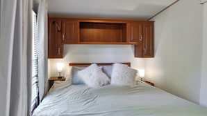 A bedroom with a bed, two bedside lamps, a wooden headboard, and a window with curtains.