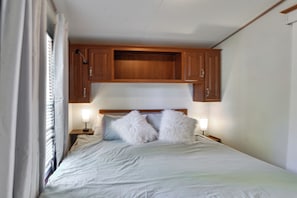 Un dormitorio con cama, dos lámparas de noche, cabecero de madera y una ventana con cortinas.