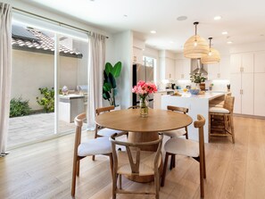 A modern kitchen with white cabinets, a round wooden dining table with chairs, and a hanging light fixture. - PGA Mediterranean Riviera Retreat. Pool & Gym Steps Away. EV, Firepit, BBQ (La Quinta)