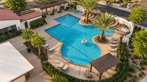 A swimming pool with a curved design, surrounded by palm trees and lounge chairs. - PGA Mediterranean Riviera Retreat. Pool & Gym Steps Away. EV, Firepit, BBQ (La Quinta)