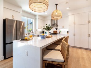 A modern kitchen with a large island, stainless steel appliances, wicker chairs, and pendant lighting. - PGA Mediterranean Riviera Retreat. Pool & Gym Steps Away. EV, Firepit, BBQ (La Quinta)