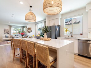 A modern kitchen with a central island, wicker chairs, a refrigerator, and a dishwasher. - PGA Mediterranean Riviera Retreat. Pool & Gym Steps Away. EV, Firepit, BBQ (La Quinta)