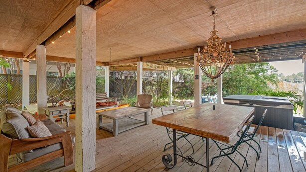 Une terrasse extérieure couverte, aménagée avec des meubles en bois, une table à manger et un jacuzzi.