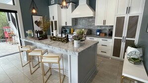 A modern kitchen with white cabinets, a marble island, bar stools, pendant lighting, and a view of the outdoors. - Stunning Indoor/Outdoor Space w/H Hills View, Pool - Casa Bonita LA (Los Angeles)