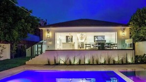 Een modern huis met een zwembad, een overdekt terras en een goed verlicht interieur.
