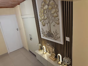 Un pasillo con una puerta blanca, un mural decorativo de un árbol y una consola con luminarias y una escultura.