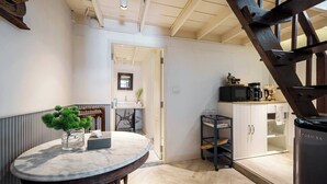 Una cocina con una mesa redonda de mármol, una silla de madera, un armario negro y una escalera.