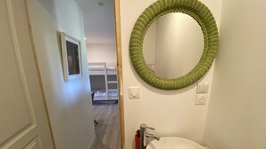 A bathroom with a white sink, a green woven mirror, and a wooden floor. - Welcome to the Duchy of Uzes, in the charming village of Ste Eulalie. (Garrigues-Sainte-Eulalie)