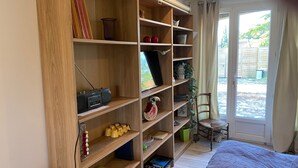 A room with a large wooden bookshelf, a bed, and a view of the outdoors through a glass door. - Welcome to the Duchy of Uzes, in the charming village of Ste Eulalie. (Garrigues-Sainte-Eulalie)