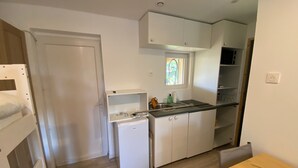 A compact kitchen with white cabinets, a small refrigerator, a window with a view, and a wooden table. - Welcome to the Duchy of Uzes, in the charming village of Ste Eulalie. (Garrigues-Sainte-Eulalie)