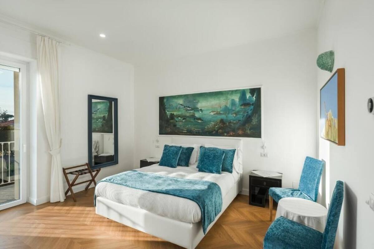 A bedroom with a bed, a painting, a chair, and a small table.