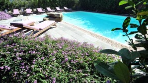 Una piscina con sillas de descanso y un jardín con flores moradas.