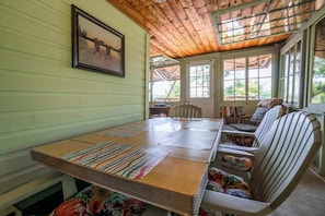 Une pièce avec une table en bois, des chaises, un tableau encadré au mur et une fenêtre donnant sur un paysage verdoyant.