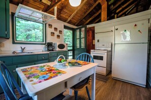Una cocina con una mesa blanca, armarios verdes, un microondas, un refrigerador y una ventana con vista a árboles.