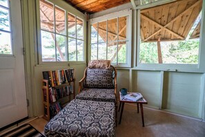 Un rincón acogedor para leer con un sillón estampado, una mesita y una estantería llena de libros.