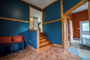 Eine Treppe mit Holzhäuschen führt zu einer zweiten Etage, eine Bank mit Kissen und eine Tür zu einem weiteren Raum.