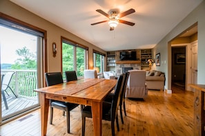 Une pièce spacieuse comprenant une table à manger en bois, des chaises, un ventilateur de plafond, une cheminée et un téléviseur.