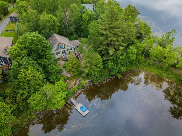 Une maison entourée d’une forêt dense et donnant sur un plan d’eau équipé d’un quai.