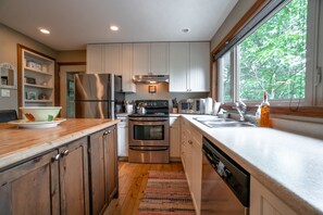 Une cuisine moderne dotée d’appareils électroménagers en acier inoxydable, de meubles en bois et d’une grande fenêtre offrant une vue sur les arbres.