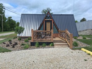 A small, modern cabin with a wooden deck and a metal roof.