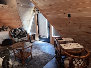 A cozy attic bedroom with a bed, a chair, a table, and a window.