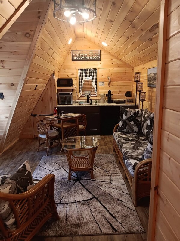 A cozy attic bedroom with a kitchenette, a dining area, and a living space with a couch and chairs.