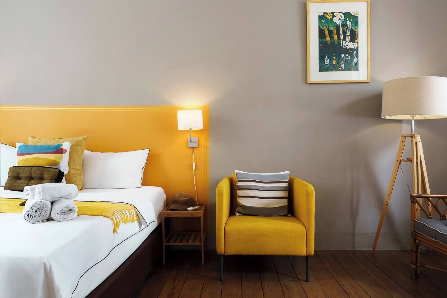 Quarto de hotel com cama, uma cadeira, mesa de cabeceira, luminária e um quadro na parede.