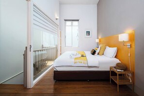 A bedroom with a bed, bedside table, lamp, and a window. - The Post · Cook, Lounge, and Stay In (Bang Rak)